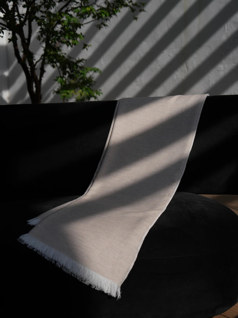 Interior drape texture shot of CHENZHI linen TENCEL wool blend khaki throw blanket on black sofa, showing delicate herringbone woven texture and loose handmade white tassel fringe detail, visible silky luster of TENCEL™, breathable linen weave and soft wool mixed touch, neatly cut natural white fringed edges, displays premium multi-fabric craft and smooth drape tactile texture for home textile product display