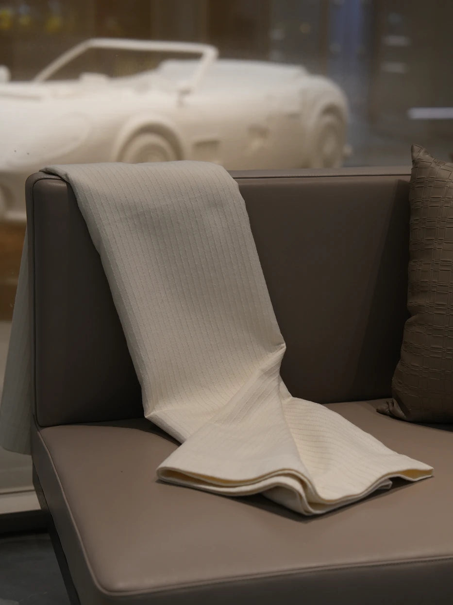 Minimalist interior still shot of folded BERLIN ribbed stripe throw placed on light coffee leather accent sofa beside floor window, soft warm contrast between pure white textured textile and warm leather furniture, lightweight soft wool blend fabric without bulky texture, great decor for entryway lounge, reading nook, hotel rest corner, warm neutral tone interior matching
