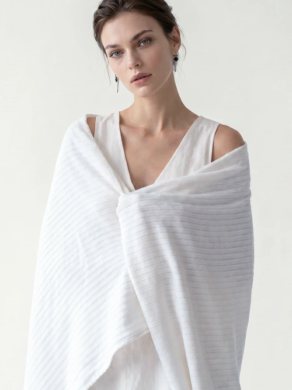 Minimalist full-body portrait shot of model fully wrapped with BERLIN white ribbed stripe throw, fully displays overall blanket silhouette, complete full-width vertical ribbed layout and neat finished edge design, dual function as decorative home couch cover and wearable shawl for indoor & outdoor use