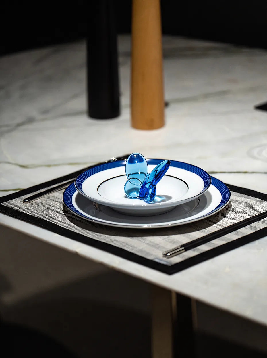Monochrome light-luxury dining furnishing shot of Klein blue butterfly placed inside double-layer blue-rim ceramic plate on light grey marble table