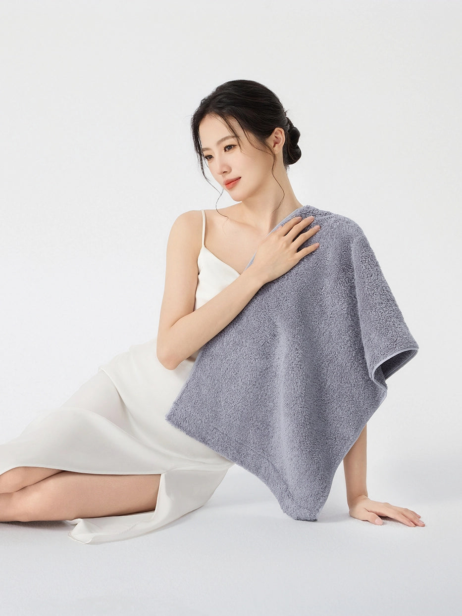 Woman sitting on floor in white slip dress, draping RESONG gray cotton terry face towel over shoulder with hand resting on towel, soft fluffy face towel gift set, white studio background