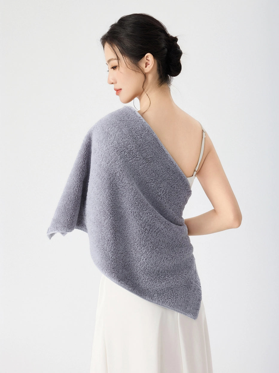 Woman in side back view draping RESONG gray cotton terry face towel over bare shoulder, soft fluffy cotton face towel on model, white slip dress, white studio background