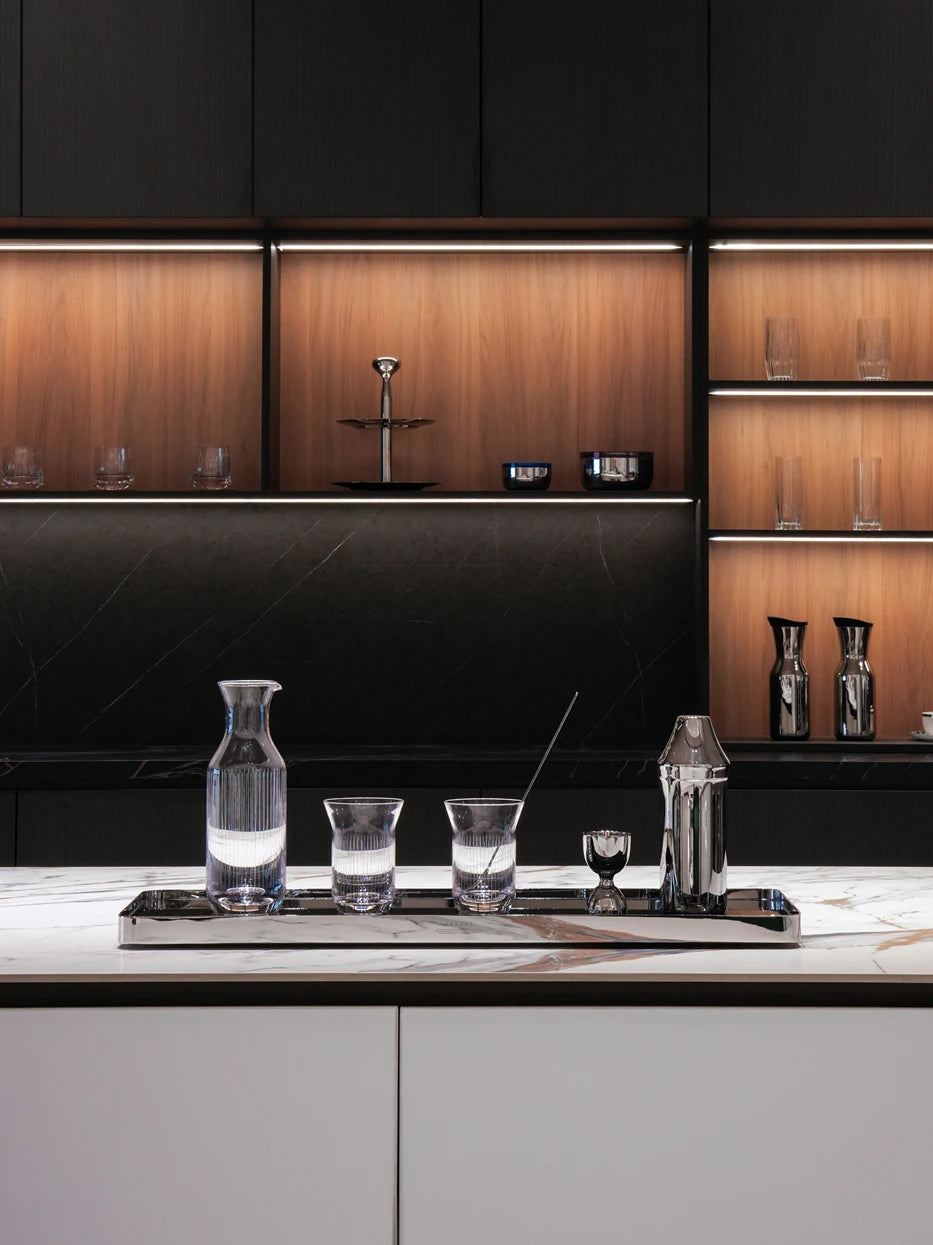 Luxury built-in bar layout shot of lengthened HD jet black L tray holding water jug, glass tumblers & bar tools on marble kitchen island