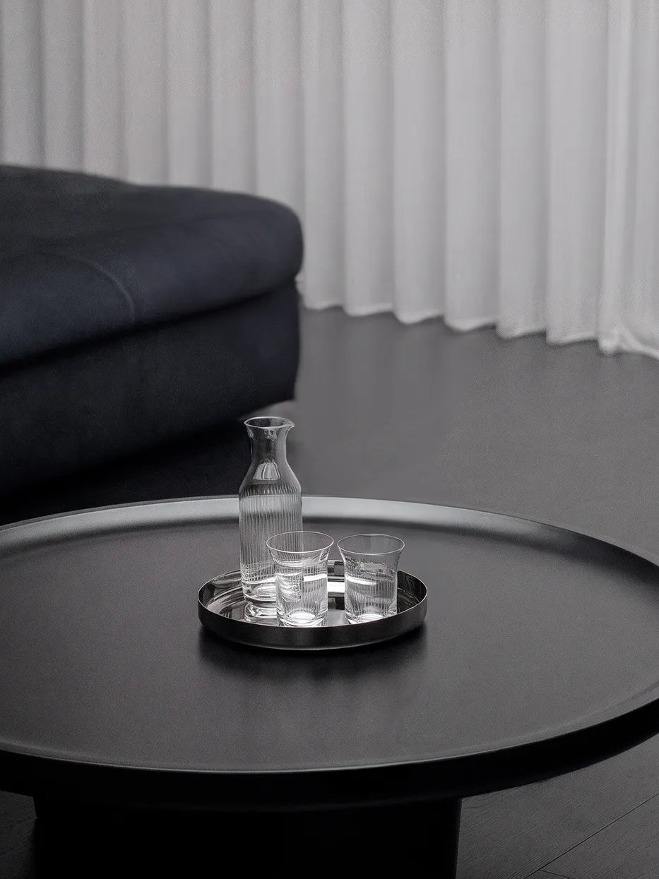 Dark minimalist home furnishing shot of HD round metal tray matched with metal vase and glass jug on black matte round stone table
