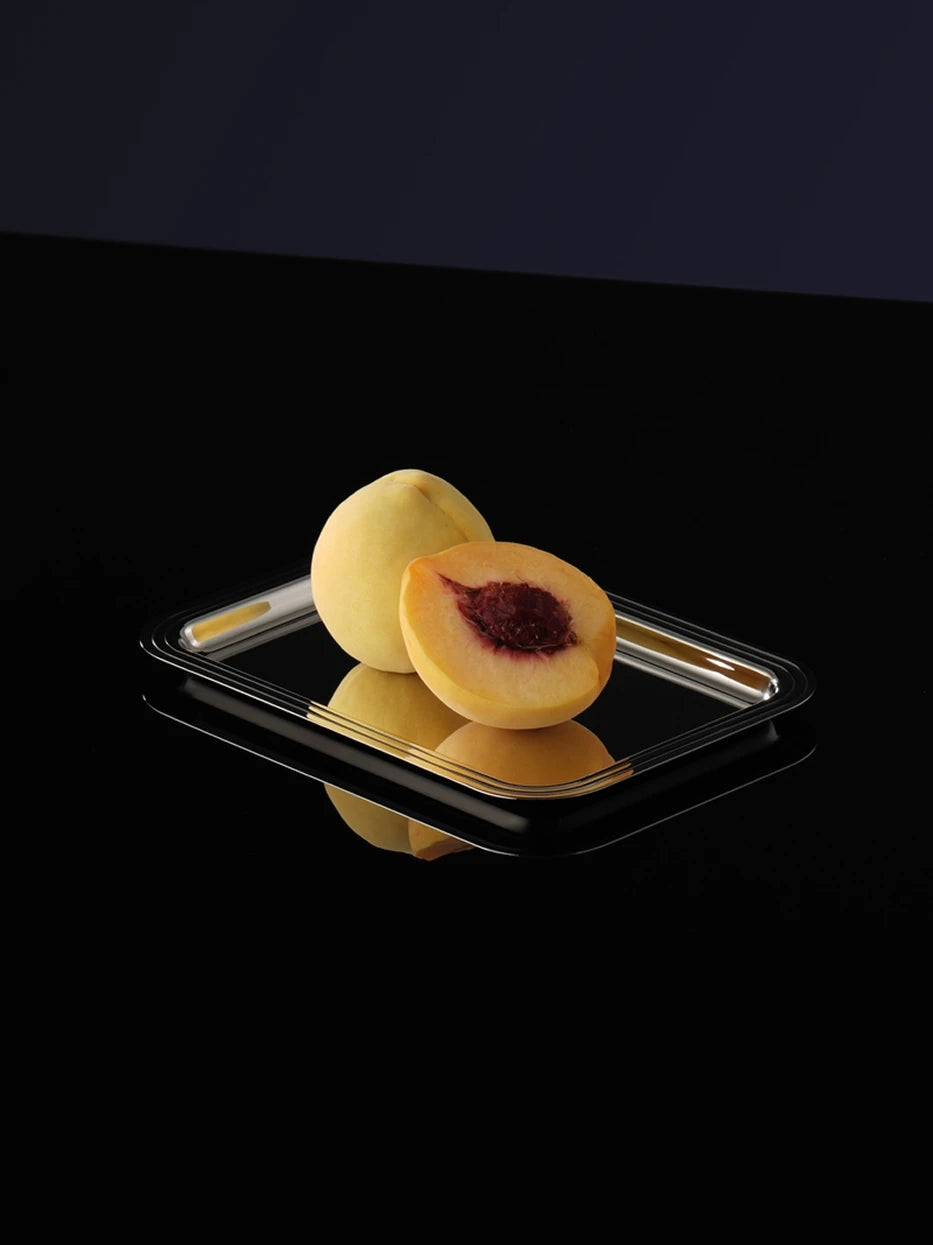 Still life close-up of HD small stainless steel tray filled with yellow peaches on glossy black reflective countertop