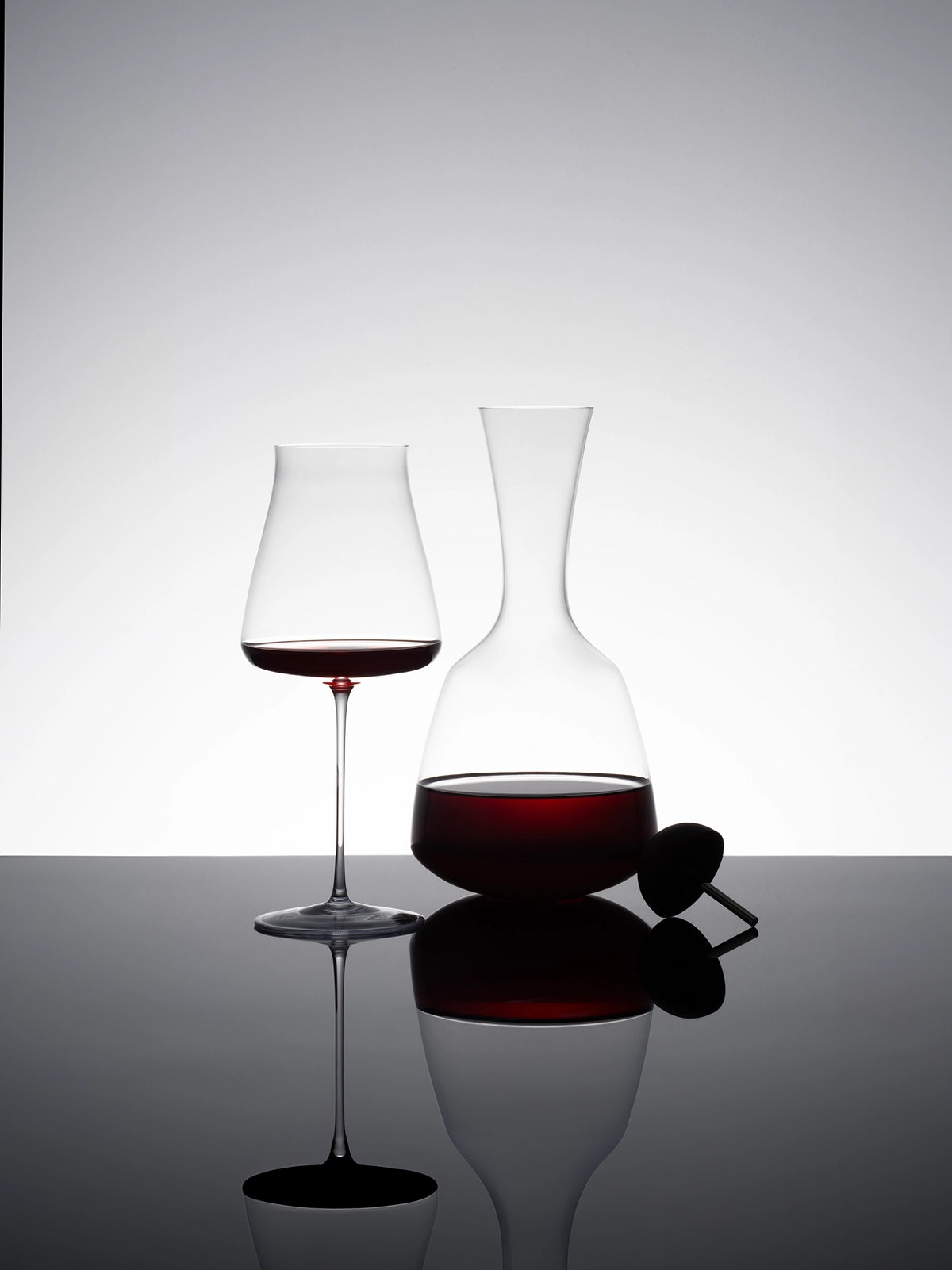 Clean studio matching set display of RESONG HOME 1833 crystal decanter paired with 1833 large bowl red wine goblet, wine stopper placed beside reflective tabletop