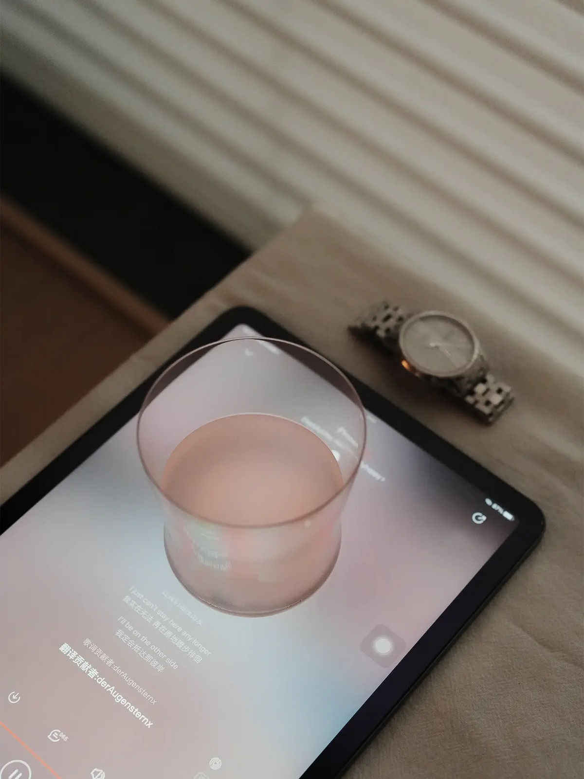 Cozy casual home lifestyle shot of RESONG HOME 1833 curved silhouette glass with pink drink, placed on tablet beside silver wristwatch, soft curtain background