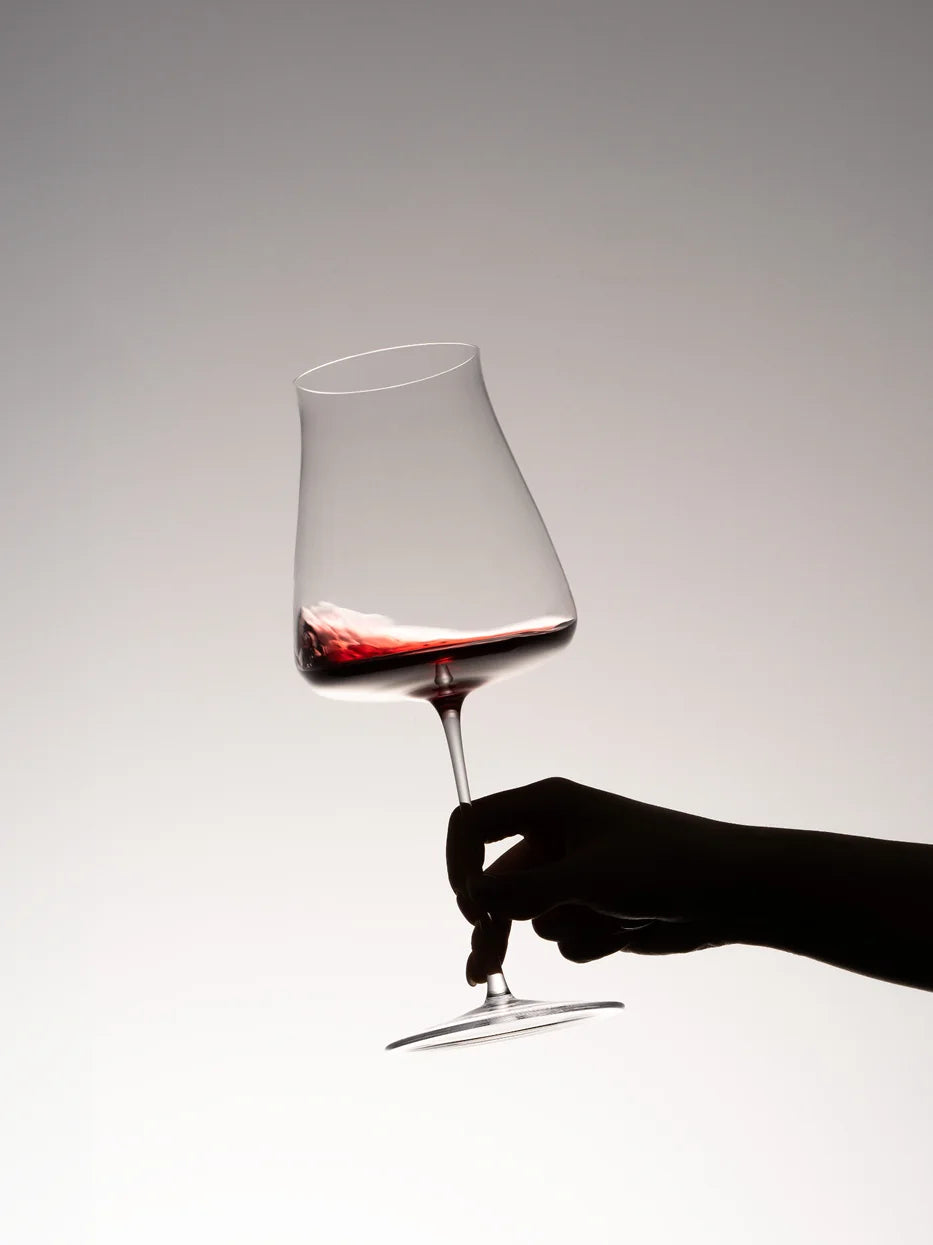 Minimal silhouette lifestyle shot of RESONG HOME 1833 large bowl crystal red wine goblet with red wine, hand swirling wine for aeration, soft grey gradient background