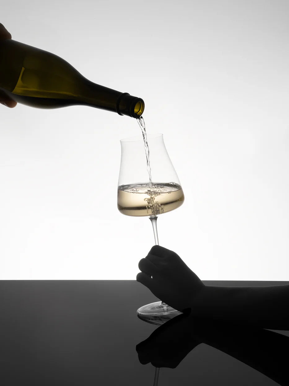 Studio product photo of RESONG HOME 1833 elegant slim white wine goblet being poured with chilled white wine, reflective black table surface