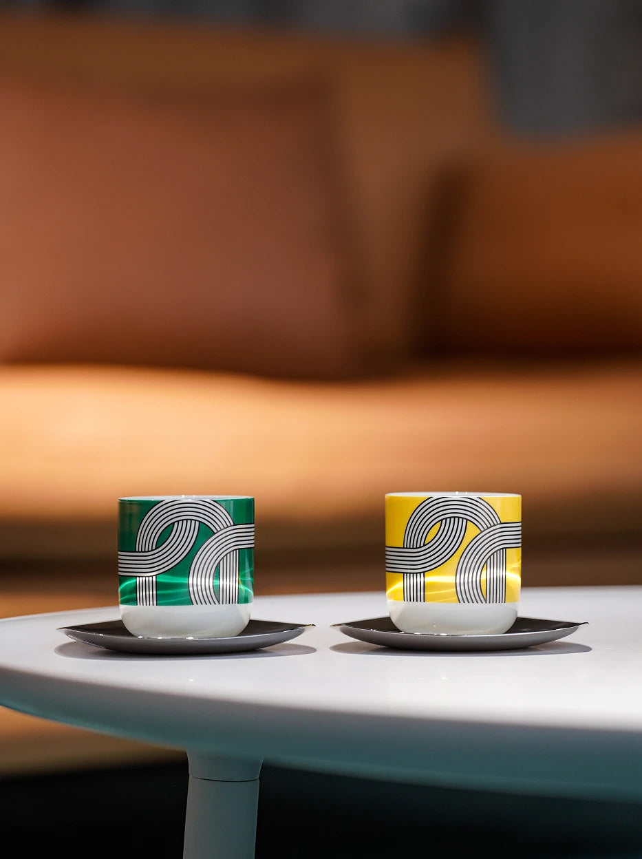 Warm living room lifestyle shot of ALK two-tone ceramic cup set on smooth white round coffee table, blurred warm brown fabric sofa as soft background