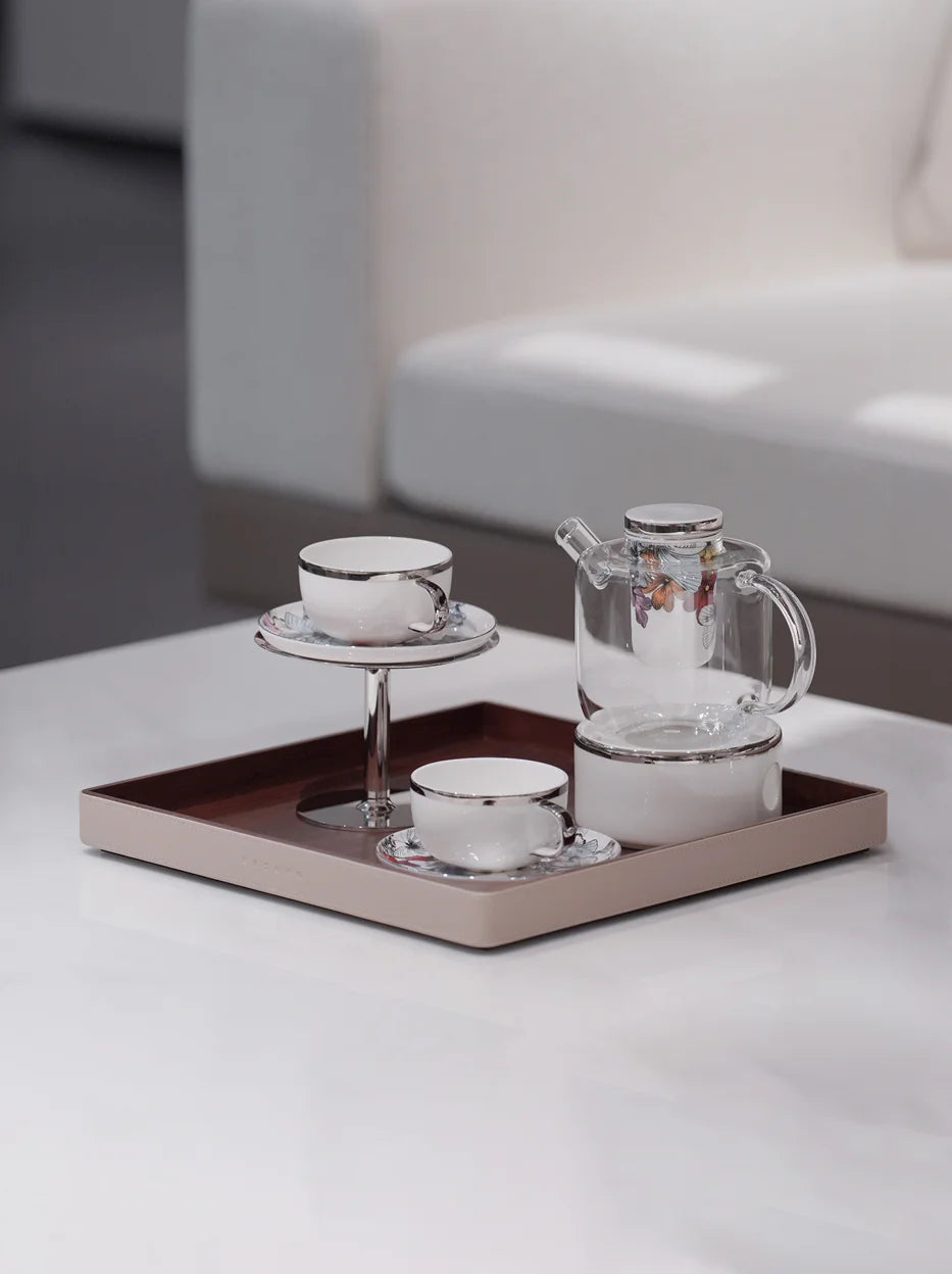 Minimal close-up studio shot of BUTTERFLY WHISPER full tea set neatly arranged on leather tray, soft light plain light table surface highlighting floral print details