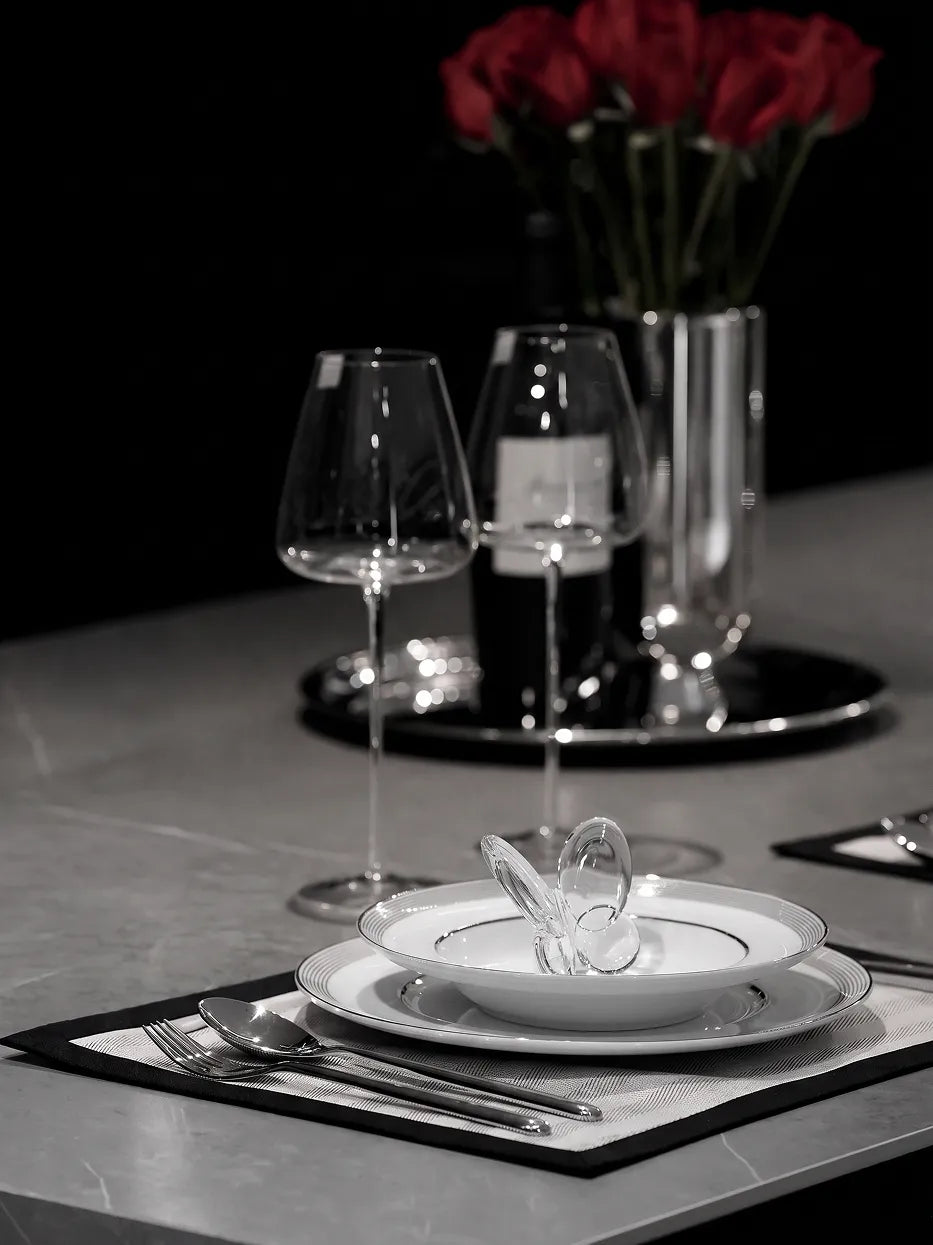 Full western restaurant table layout shot of ERYA black deep plate set with vertical striped wine goblets, glass decanter and red rose flower arrangement on grey marble counter