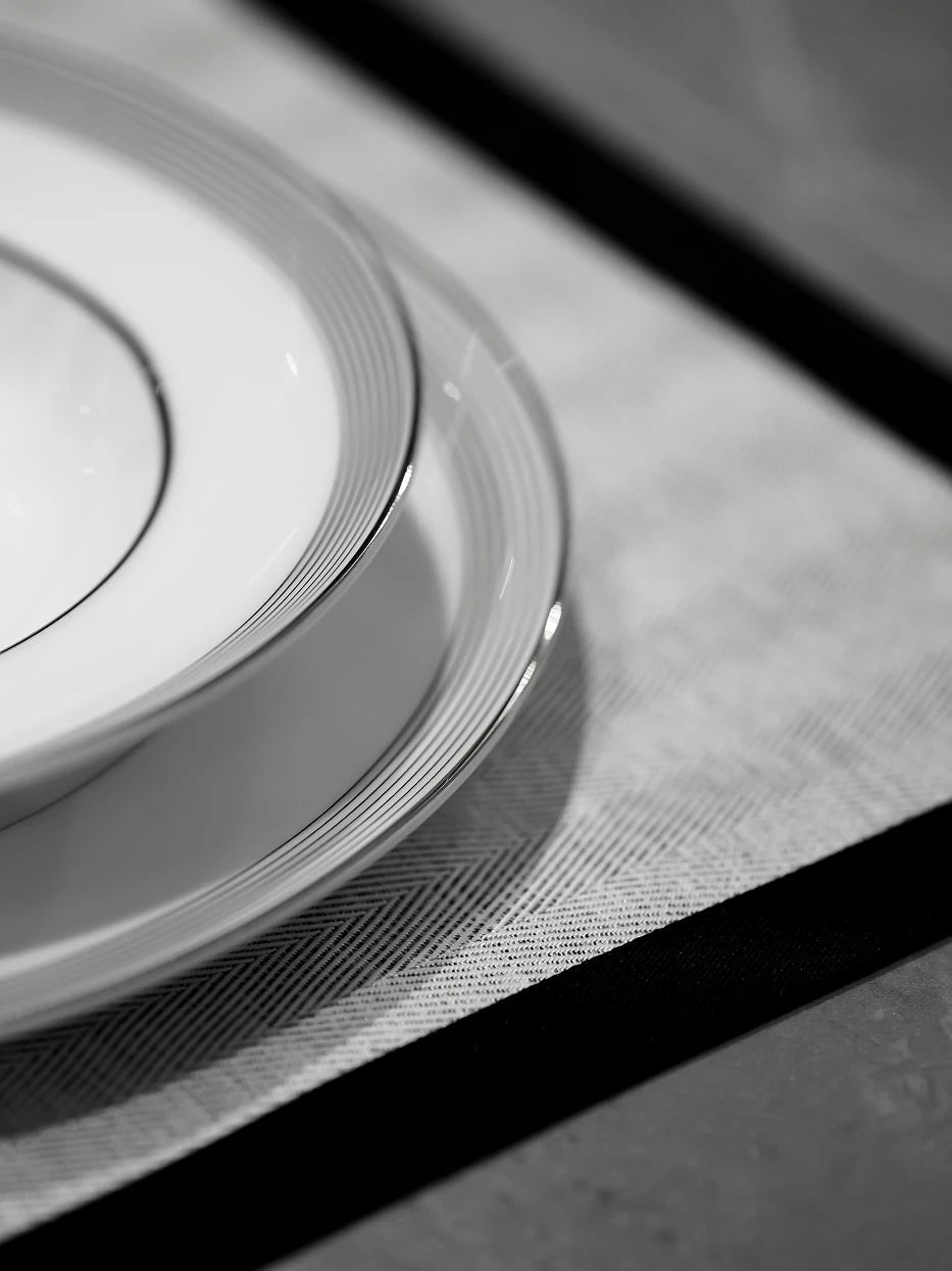 Monochrome minimalist close-up still life of stacked ERYA black rim deep plate set, focusing on delicate gradient silver-black concentric lines and glossy porcelain glaze