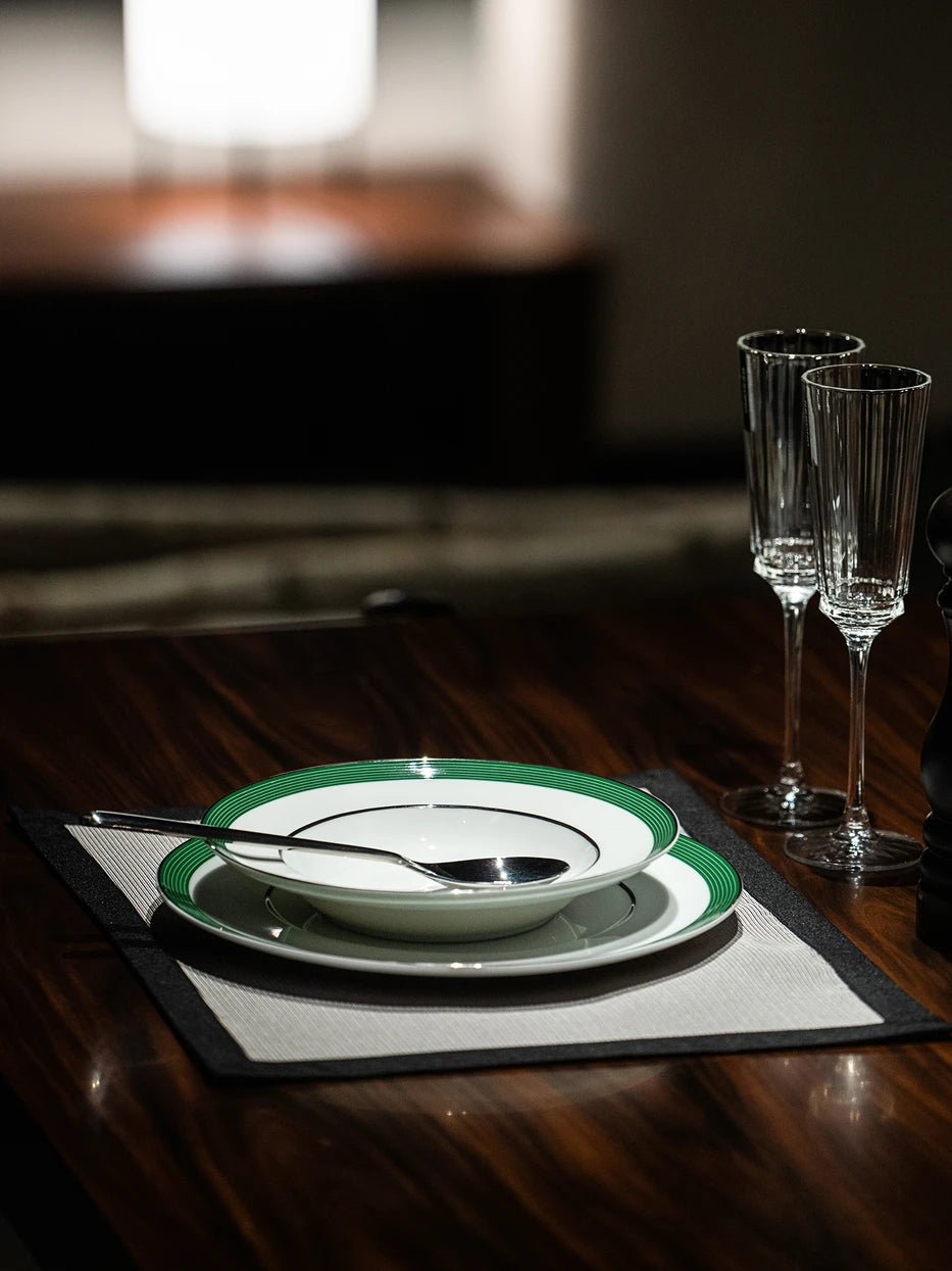 Home dining layout shot of ERYA green rim deep plate matched with metal spoon and vertical striped champagne flutes on dark wood tabletop