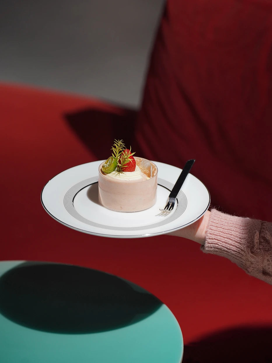 Dessert afternoon tea shot of ERYA medium black-silver plate holding fruit mousse cake with mini silver dessert fork, warm red solid backdrop for striking color contrast