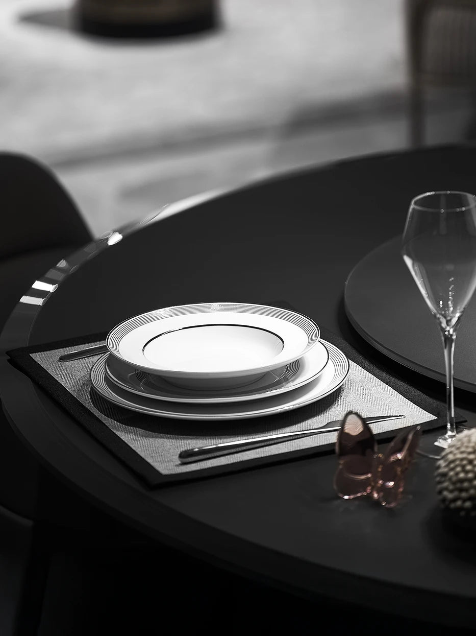 Atmospheric western table layout shot of stacked ERYA medium & large black-silver plate set, matched with rose gold butterfly ornament and tall wine goblets on matte black round glass table