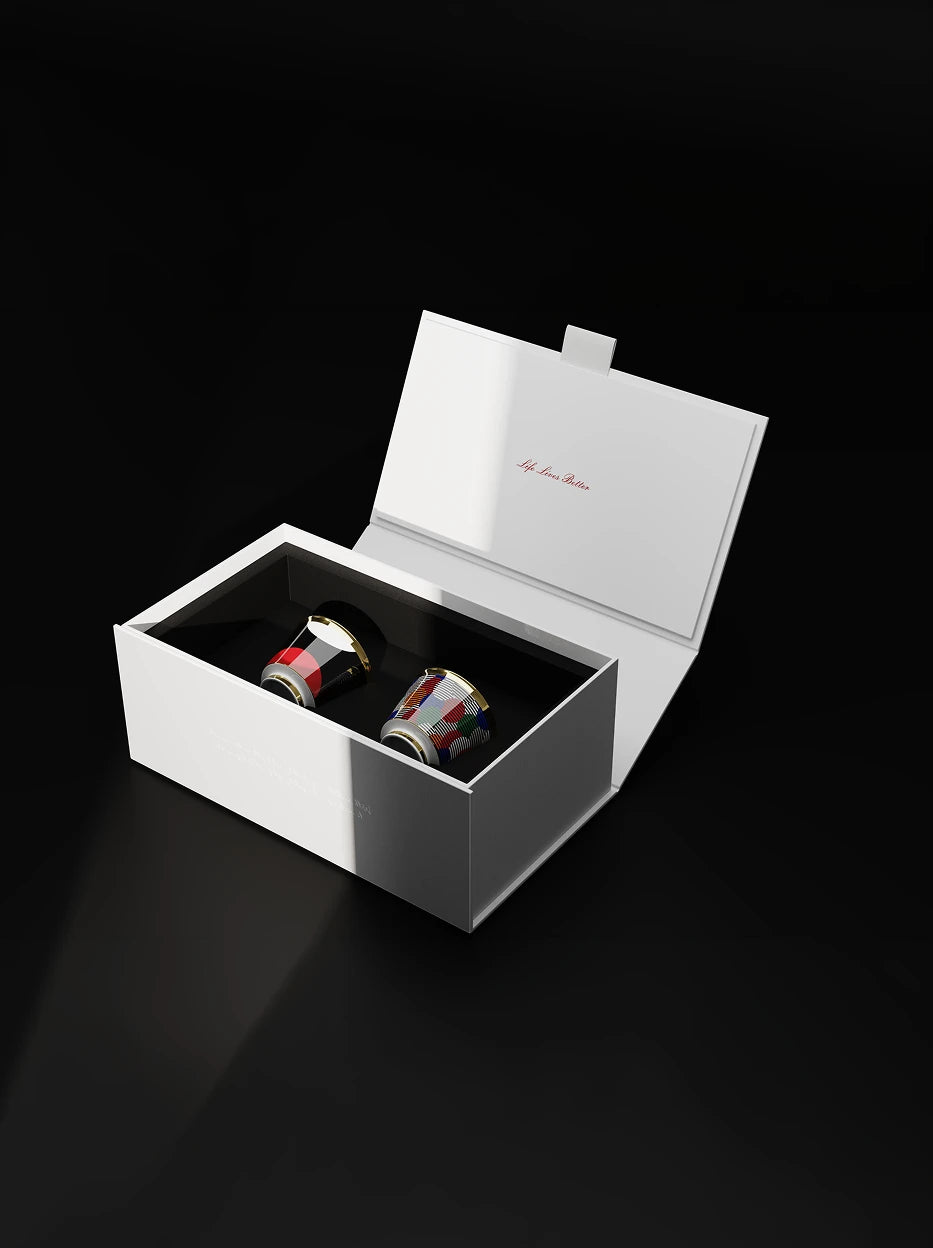 Premium dual-cup unboxing shot, Composition and Sunrise gold-rim cups embedded side by side in black flocking lining of branded white flip gift box, solid pure black minimalist background