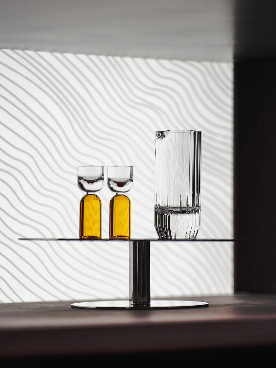 Modern minimalist lifestyle shot of HAOYING amber baijiu crystal set on single-tier metal display stand, wavy textured white wall background