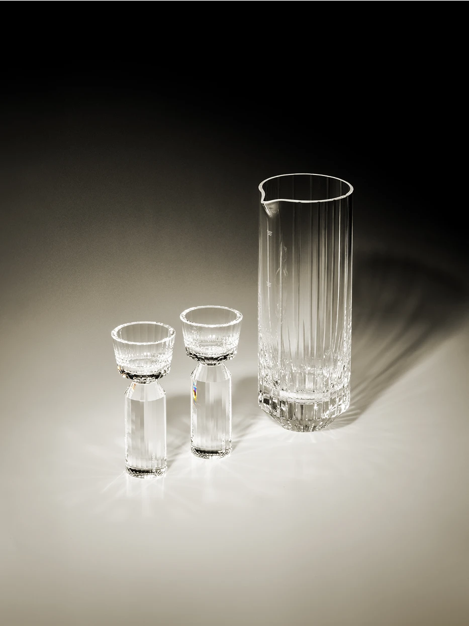 Soft gradient tone studio display of HUAZUN clear crystal baijiu serving set, warm side natural light casting striped refracted shadows to highlight hand-carved vertical facets