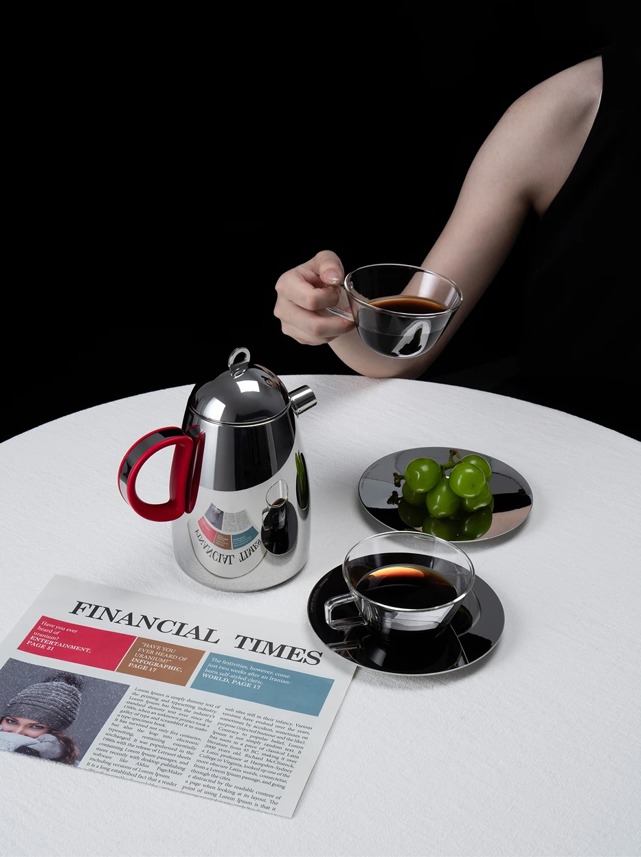 Minimal monochrome studio still life of KELUO stainless steel pot and glass cups, laid with financial newspaper and fresh green grapes on smooth white tabletop