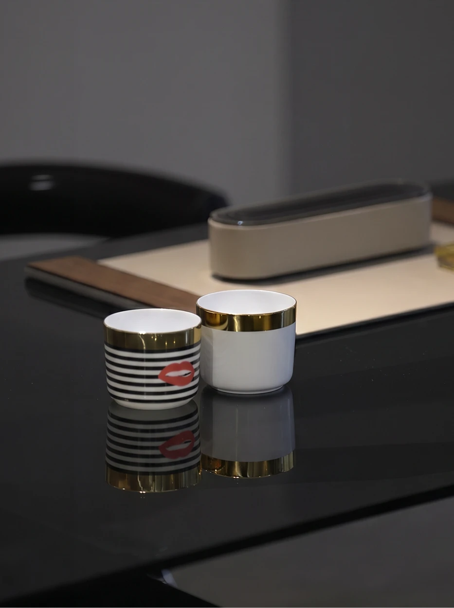 Minimal interior shot of two POP Art gold-rim cups placed on glossy black tabletop, leather storage box as background decor