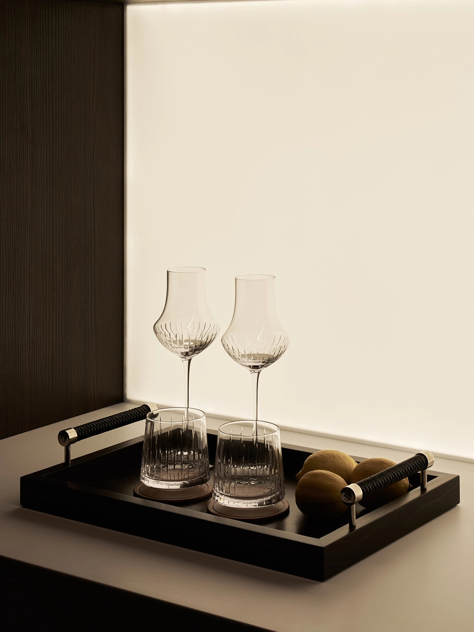 Warm lifestyle interior shot of RESONG TRIUMPH crystal glass set placed on black wooden handle tray, decorated with fresh lemons beside light wall