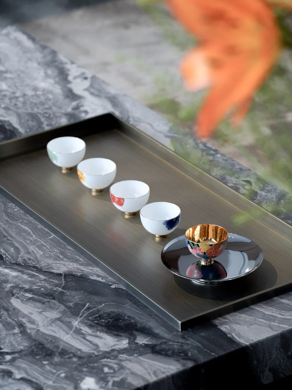 New Chinese-style tea room lifestyle shot of the five floral tea cups neatly arranged on rectangular metal tea tray, white marble tabletop with blurred orange foliage foreground