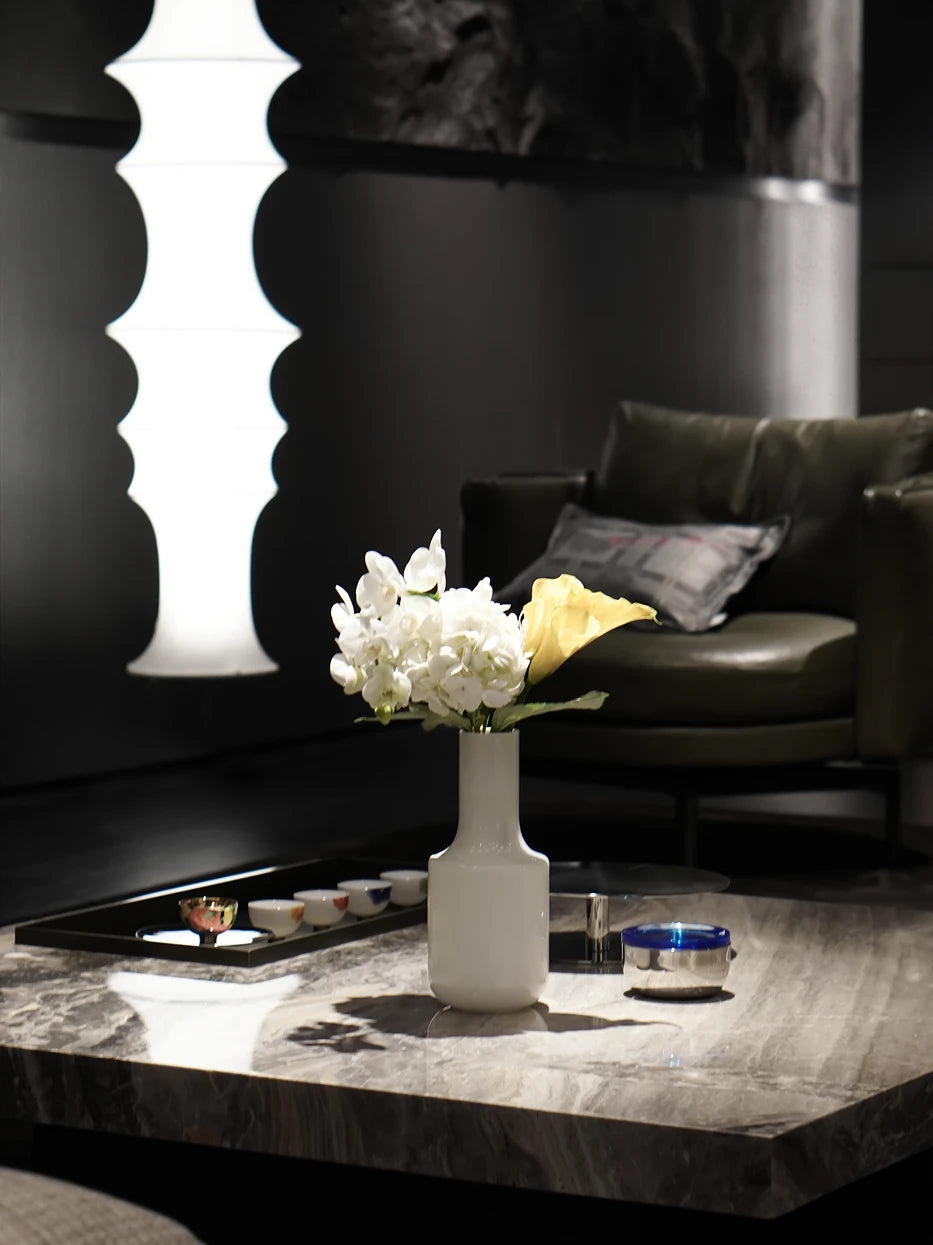 Monochrome minimalist living furnishing shot of white minimalist vase A with white orchid & yellow calla on light grey marble coffee table