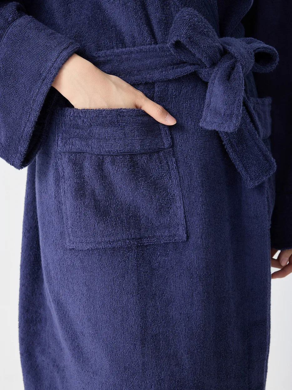 Close-up of RESONG navy blue hooded terry cloth bathrobe showing patch pocket, matching belt tie and cuff detail, hand resting in pocket, soft absorbent cotton texture, white background