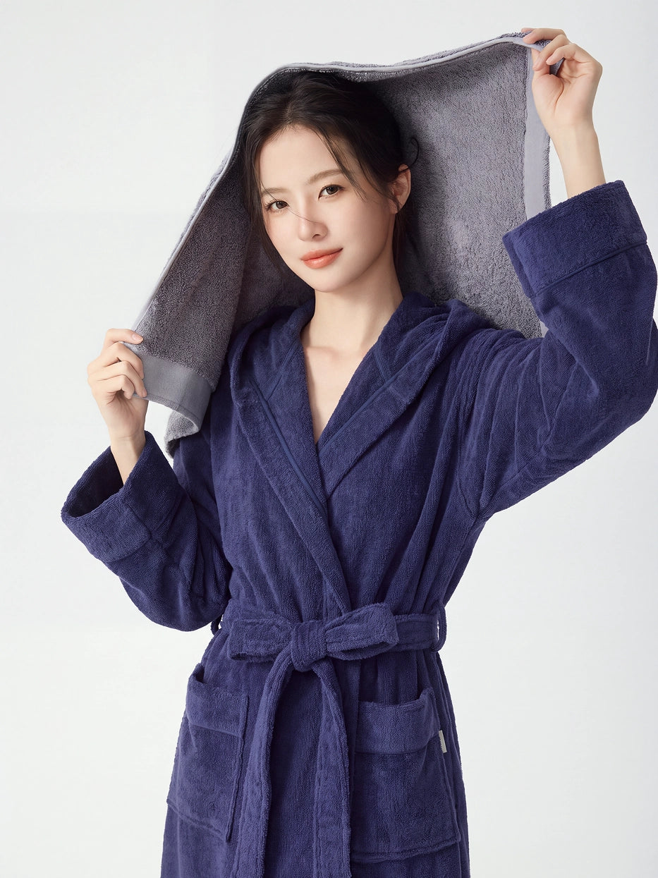 Woman wearing RESONG navy hooded terry cloth bathrobe holding a grey cotton bath towel overhead, luxury bath towel and bathrobe gift set