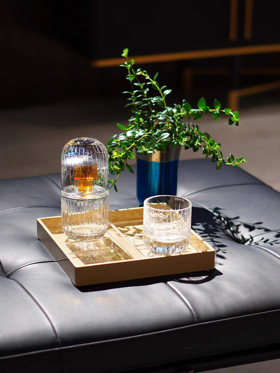 Minimal tea room furnishing shot of khaki four-grid tray on black leather ottoman matched with glass tea set & green foliage