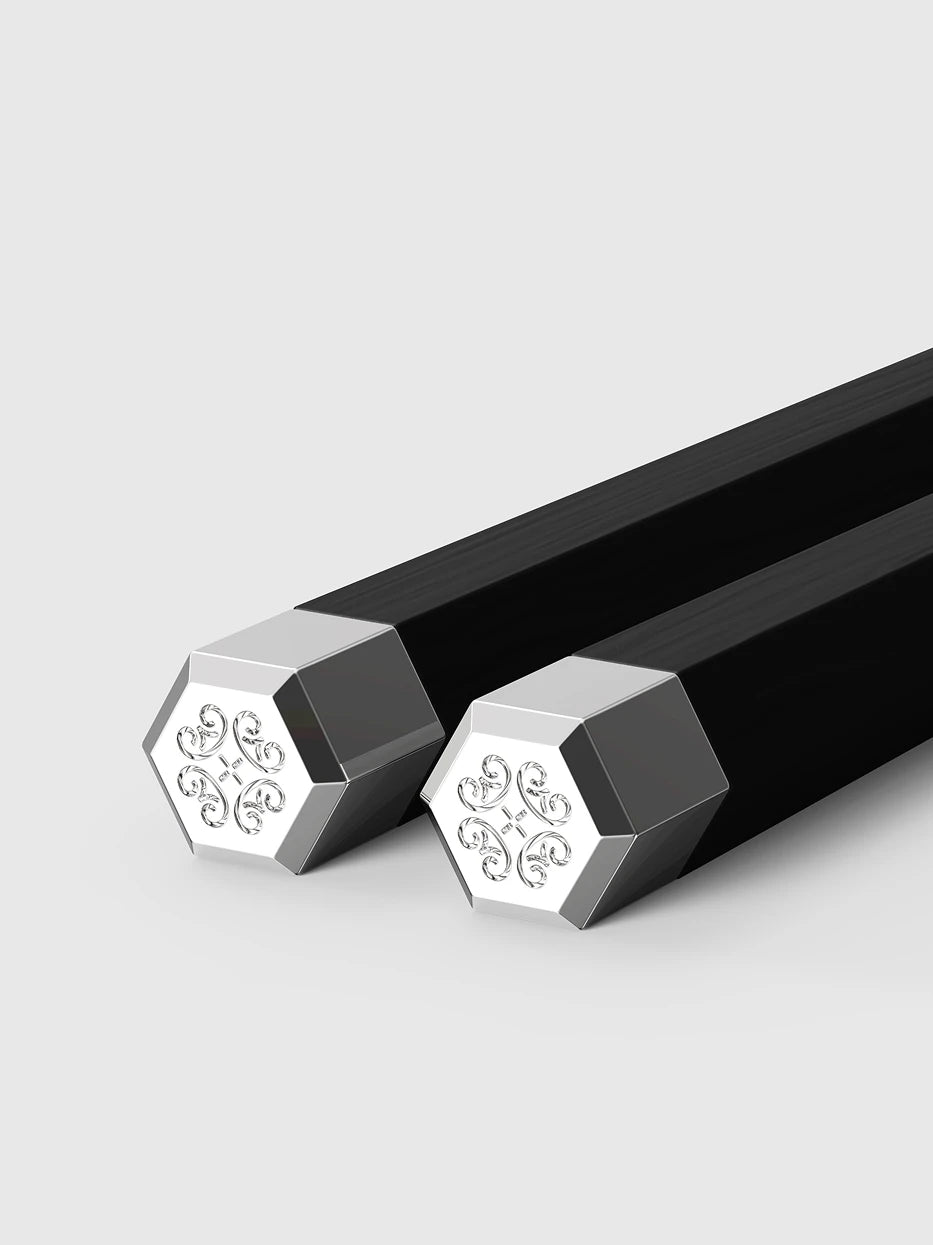 Close-up craft detail shot of hexagonal silver-plated tip of PAVILION ebony chopsticks, clear embossed traditional four-leaf scroll pattern on plain light grey background