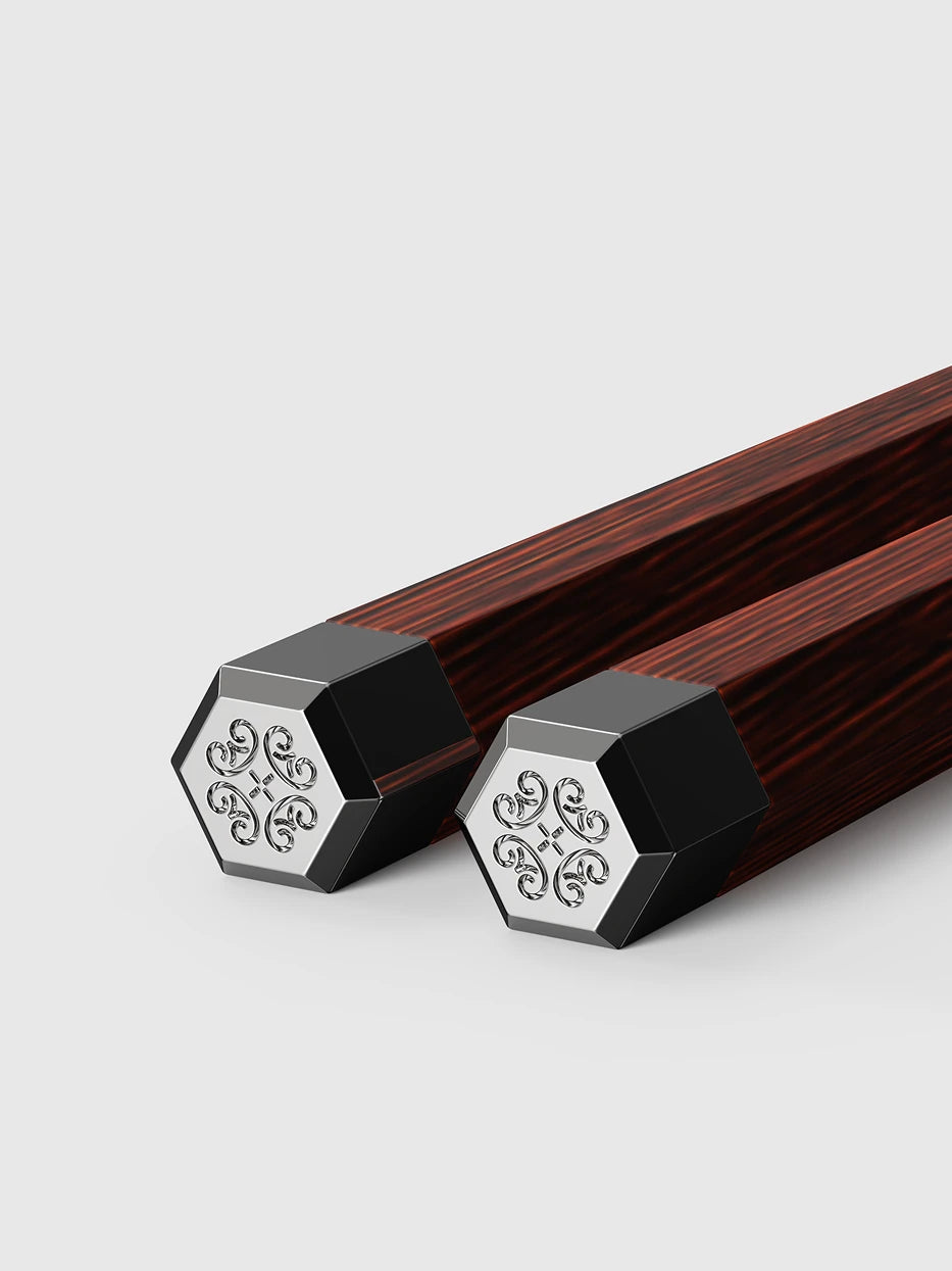 Close-up detail shot of hexagonal alloy tip of PAVILION chopsticks, embossed traditional four-leaf clover scroll pattern, plain light grey background showing delicate emboss craft
