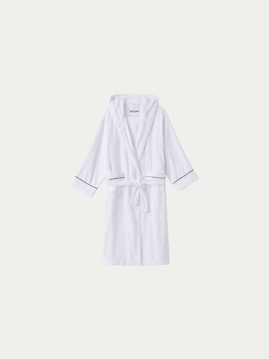 Official hanging product shot of R Collection white hooded bathrobe with navy piping on pure off-white background, 100% thick high-density cotton terry fabric, integrated three-dimensional hood, kimono V-collar, matching fabric wide waist tie, dual large side patch pockets, thin navy contrast piping on cuffs, 120cm long premium water-absorbent bathrobe for hotel and homestay use