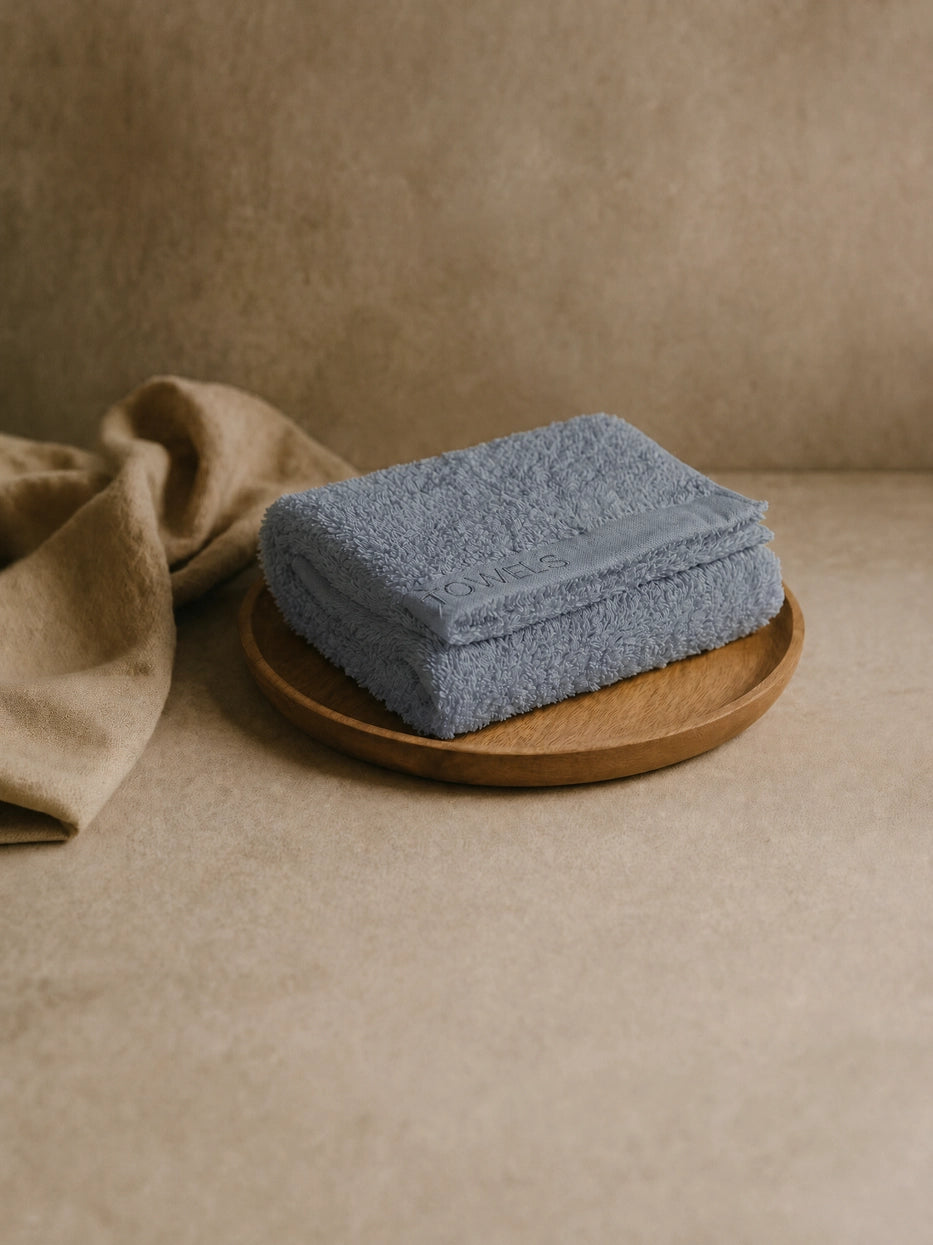 Wabi-sabi still life shot on beige micro-cement countertop with wooden tray, folded grey R Collection cotton face towel matched with linen fabric, soft natural light creates minimalist neutral bathroom atmosphere, shows interior display matching effect