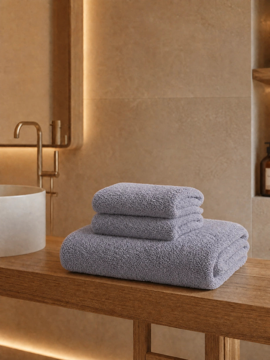 Wabi-sabi warm wood bathroom still life shot of three stacked grey towels on wooden countertop, unified solid grey tone calm and premium, matched with linear ambient light to show minimalist high-end display texture of full gift set