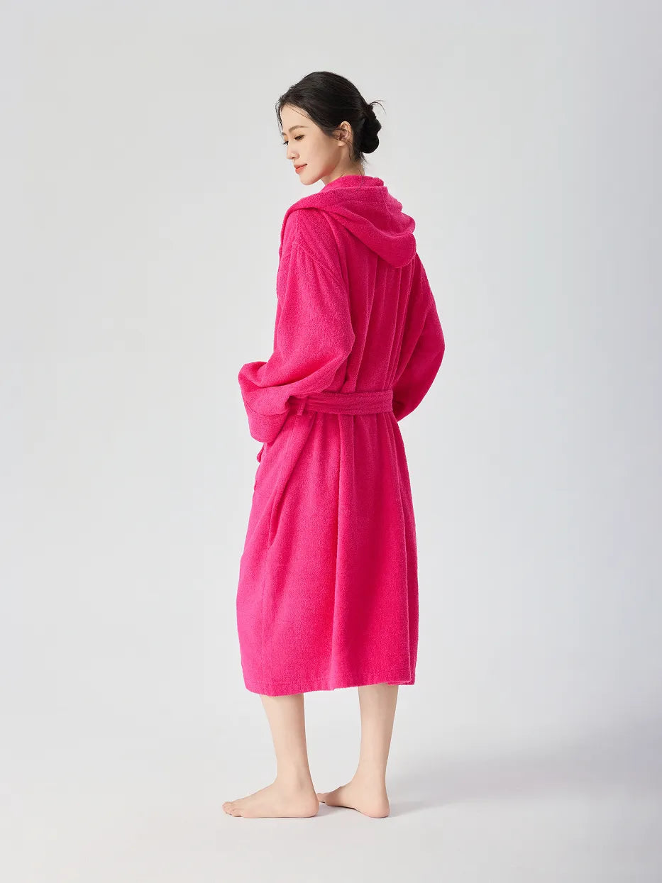 Barefoot woman standing back view wearing RESONG rose red hooded terry cloth bathrobe, showing hood back and belt tie at waist, long relaxed fit, white studio background