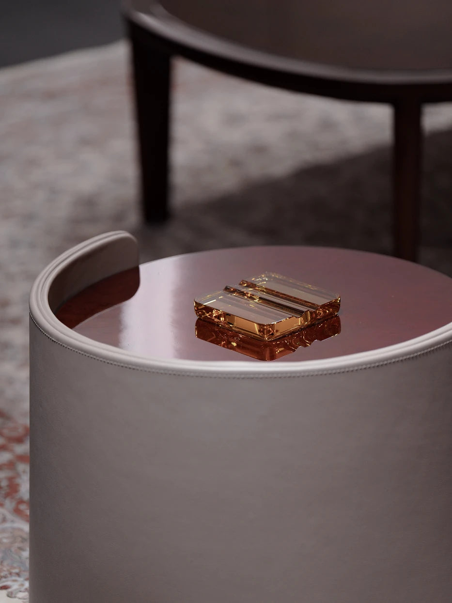 Luxury still life close-up of amber crystal cigar holder on rose gold glossy round stool, side light highlighting warm transparent amber luster