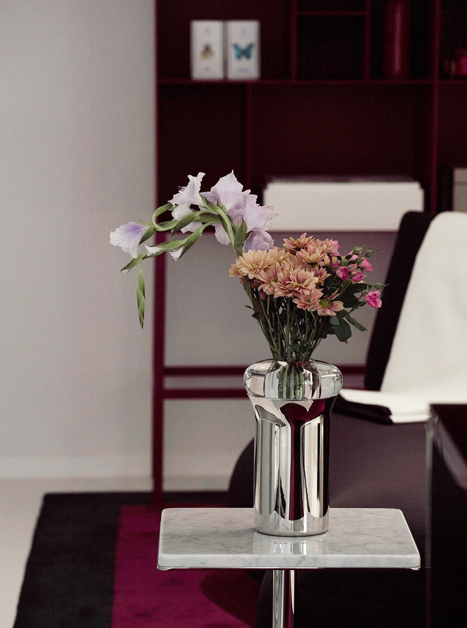 Soft minimalist living furnishing shot of SHEDI double-wall vase with pink & purple eustoma on narrow white marble side table beside dark wood bookcase