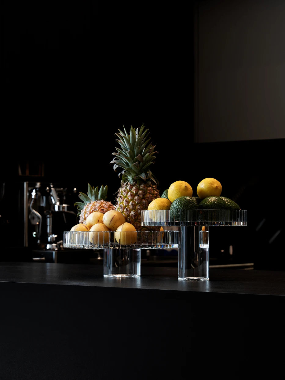 Commercial display shot of SHIJI M crystal fruit plate filled with pineapples, avocados and fruits on dark stone bar counter