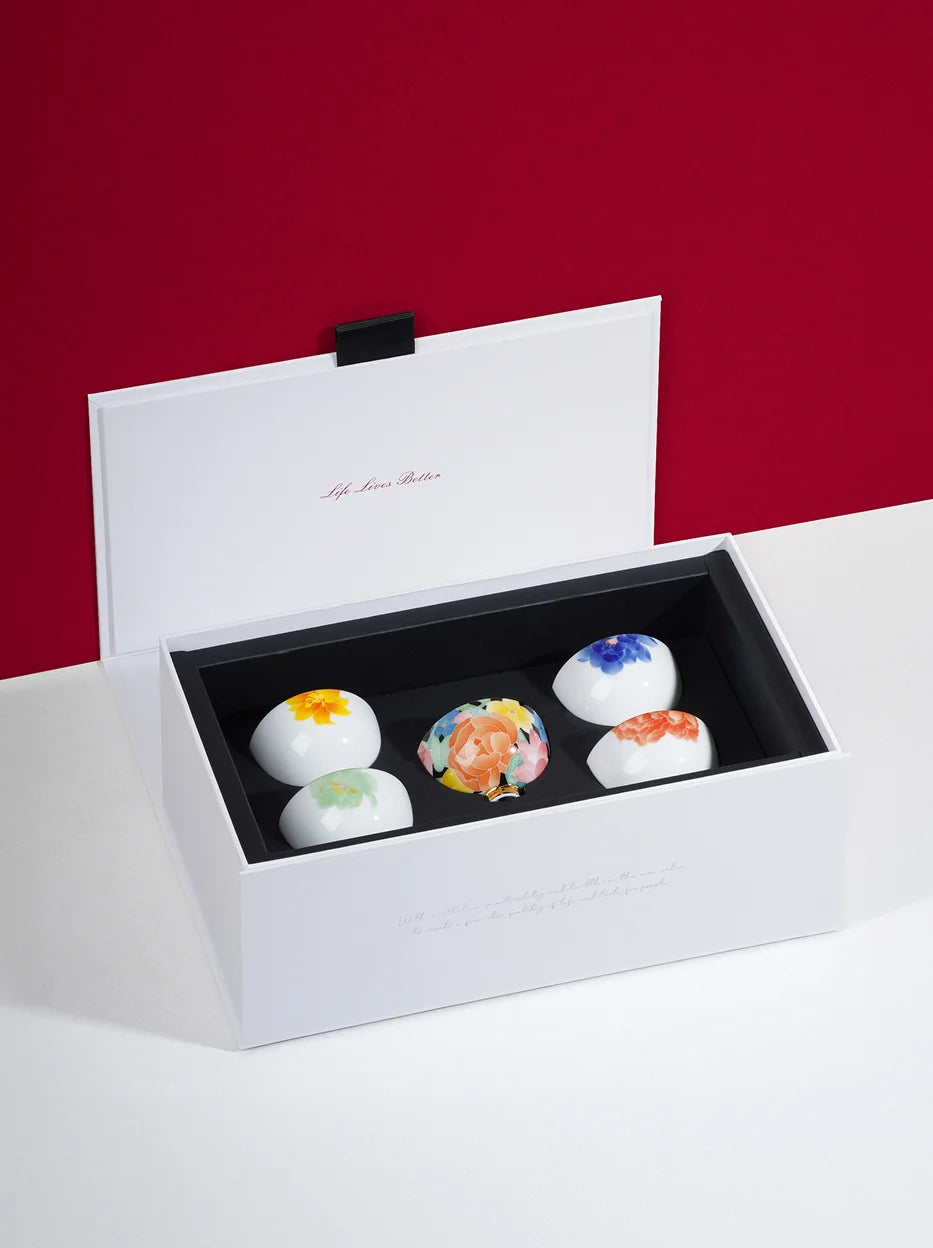 Full interior shot of opened gift box for RESONG UNDERGLAZE MULTICOLORED ceramic cup set, five teacups with unique hand-painted floral patterns fixed in black flannel lining, minimalist red background premium tea gift packaging display