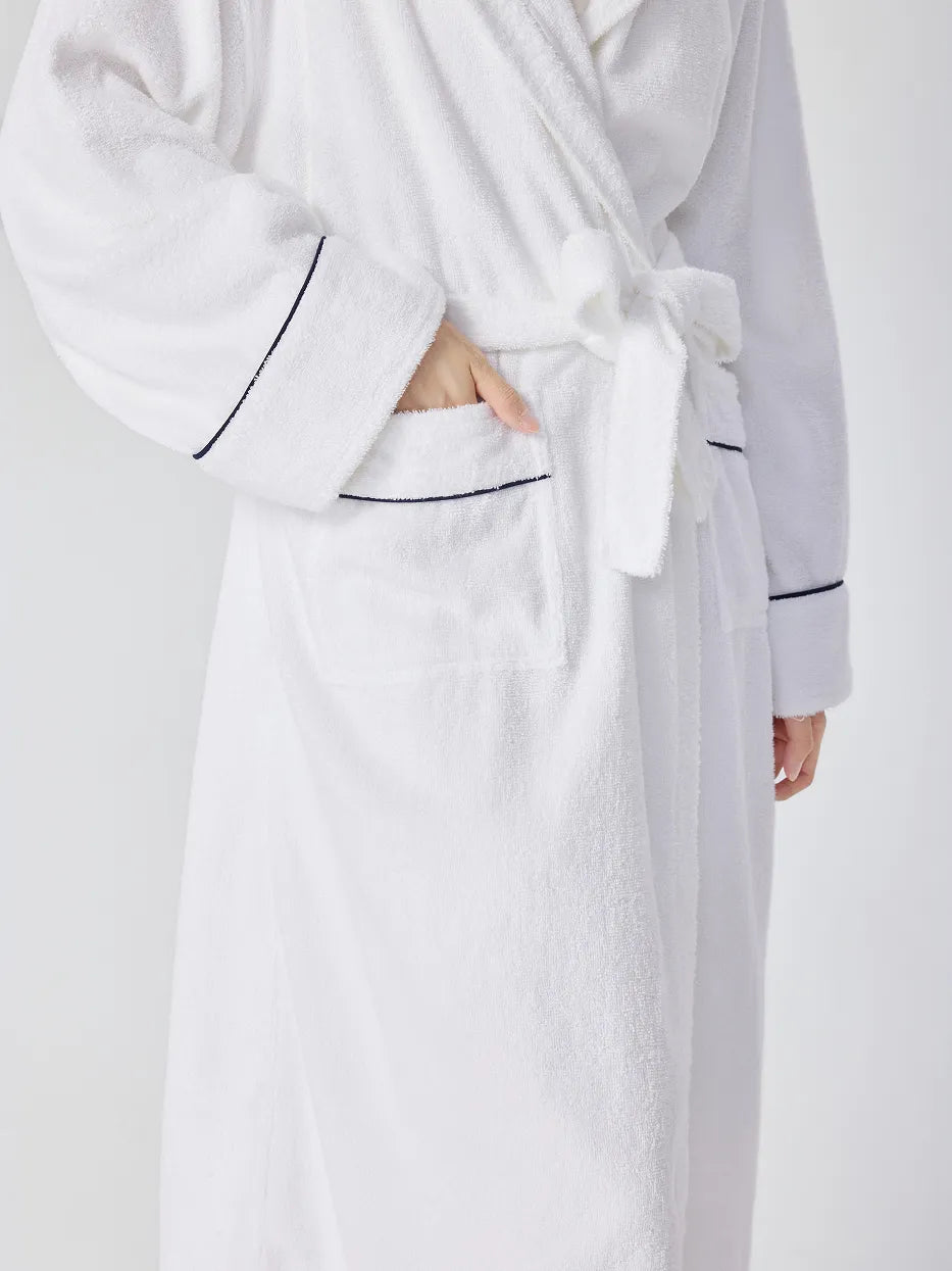 Close-up of RESONG white hooded terry cloth bathrobe showing patch pocket with navy piping, matching belt tie and cuff trim, hand resting in pocket, soft absorbent cotton texture, white background