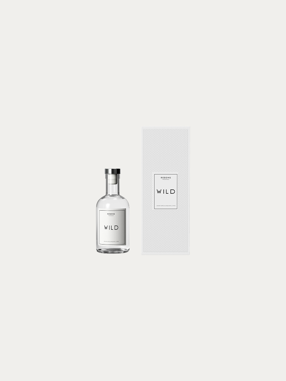 Official product shot of WILD aromatherapy set with essential oil bottle & textured white gift box on pure off-white background, short rounded transparent glass bottle with silver metal cap, minimalist black-white label, complete gift aromatherapy kit