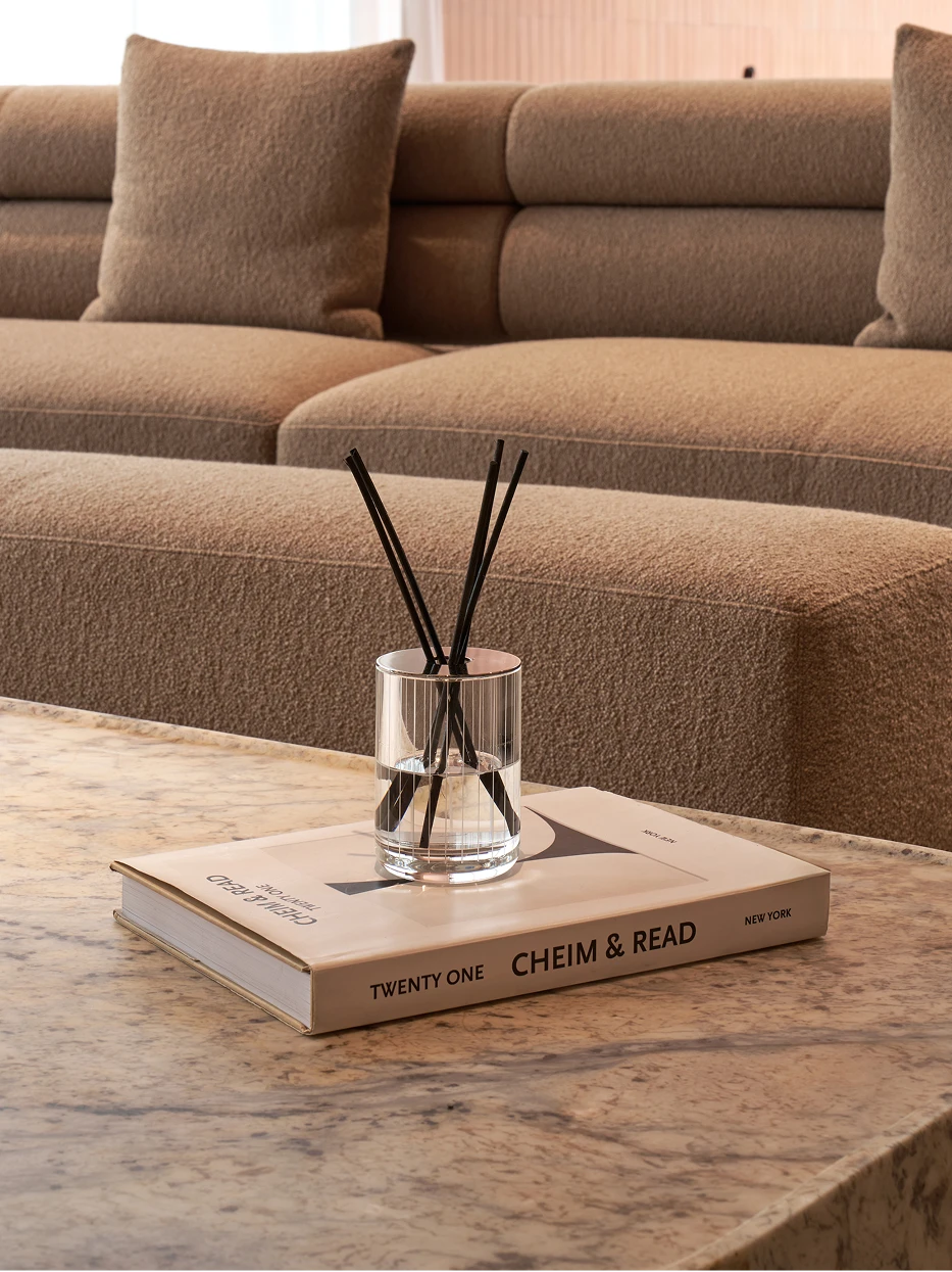 Cream minimalist living furnishing shot of XUYU crystal diffuser on hardcover decor book over light grey marble coffee table