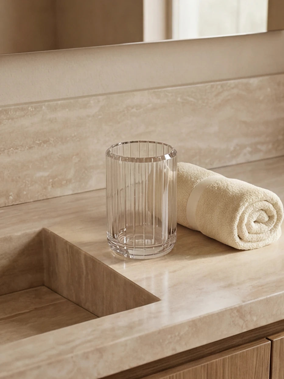 Cream wood bathroom furnishing shot of single XUYU striped crystal cup beside folded beige towel over travertine countertop