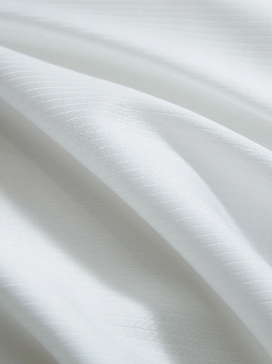 Soft light close-up shot of YALIAN white cotton fabric, showing even delicate vertical mini jacquard stripes, tight high-density weaving