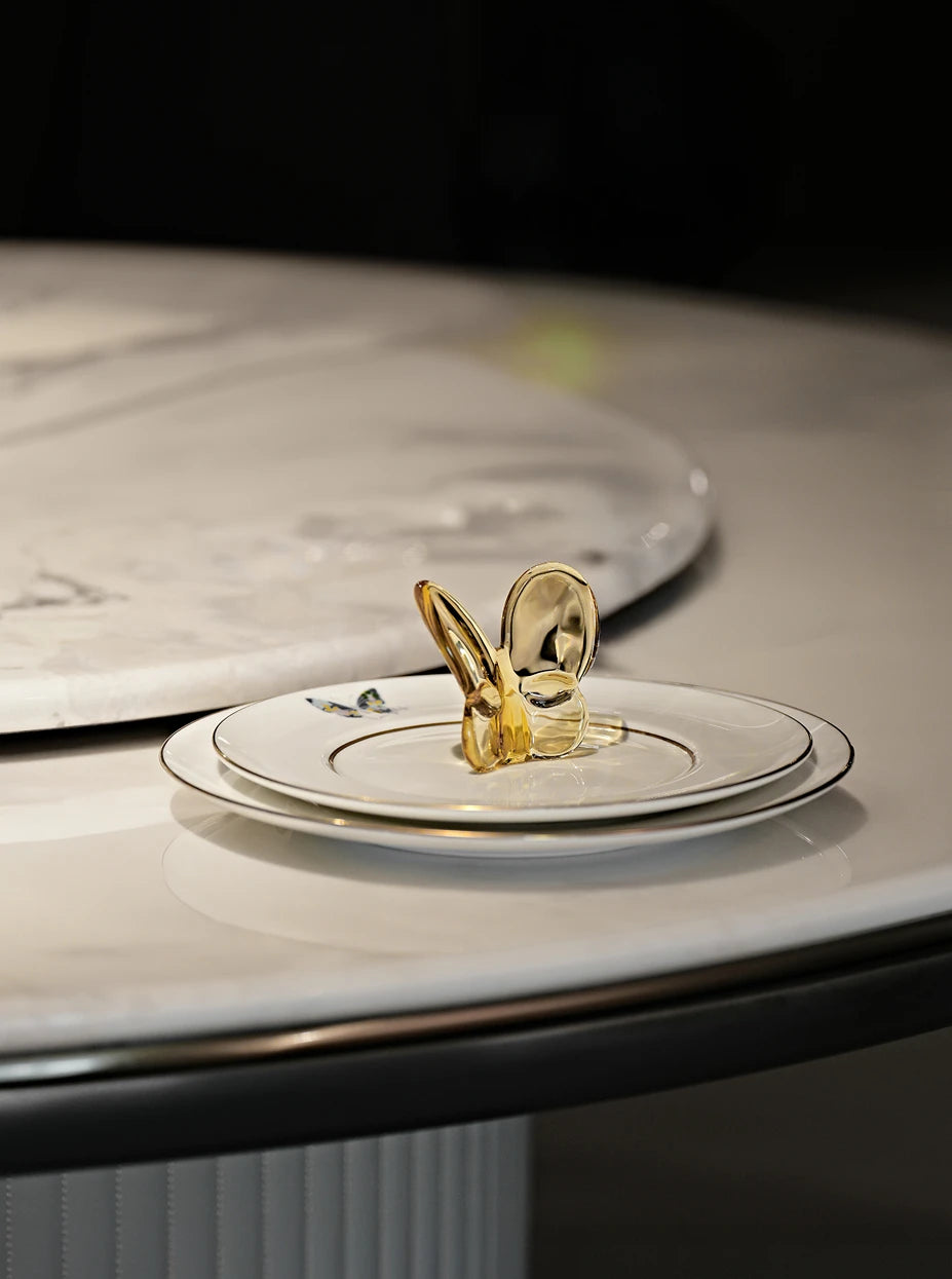 Minimalist dining furnishing shot of amber butterfly placed on double-layer gold-rim ceramic plates on marble round dining table