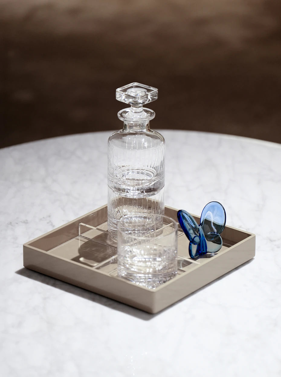 Light minimalist furnishing shot of Klein blue crystal butterfly matched with striped glass bottle on beige matte marble square tray