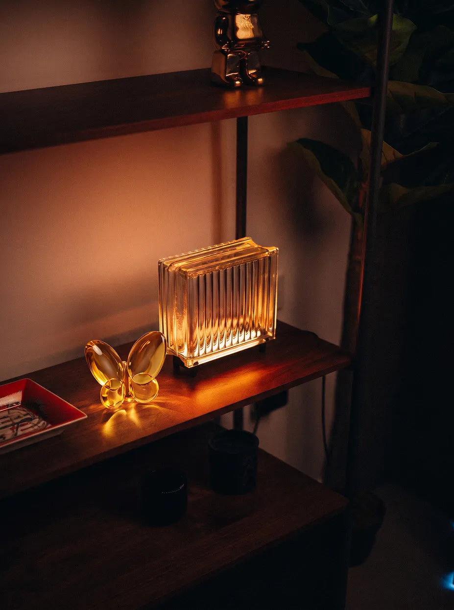Official lifestyle image of the RESONG Butterfly Ornament - Amber, a sculptural amber glass butterfly ornament styled on a shelf in a modern interior.
