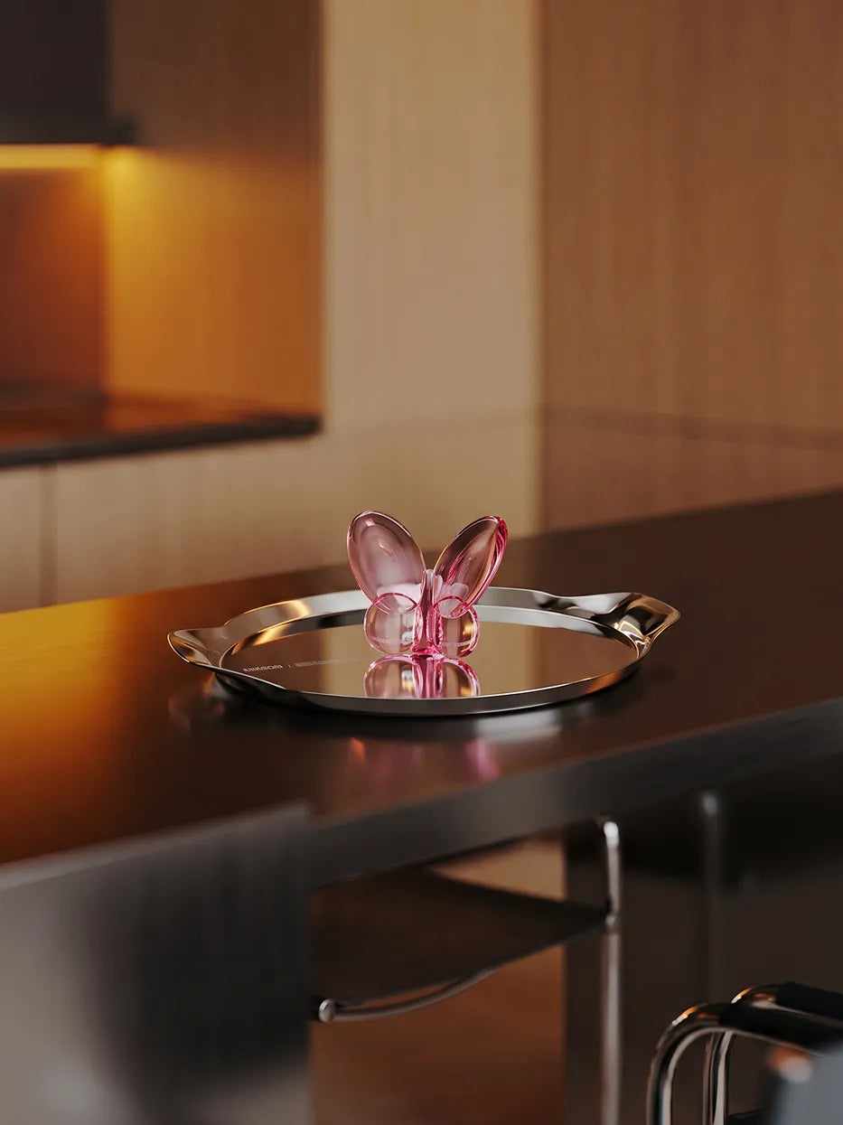 Official lifestyle image of the RESONG Butterfly Ornament - Pink, an elegant pink glass butterfly decorative sculpture displayed on a stainless steel tray in a contemporary home setting.